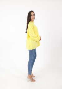 Maglione giallo oversize in maglia con spalle scese, abbinato a jeans aderenti blu e sandali trasparenti con tacco a blocco.