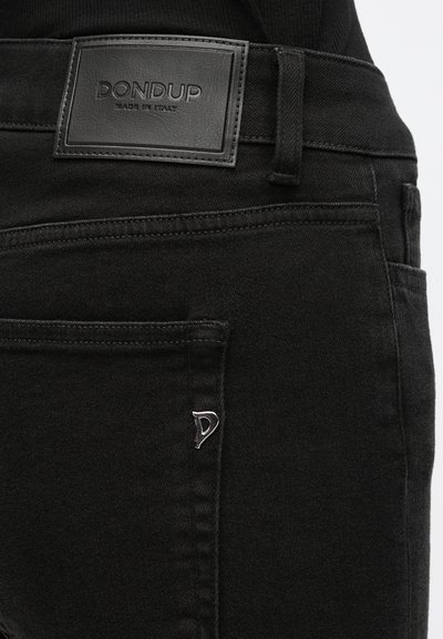 Κοντινή λήψη μαύρων τζιν από τζιν υλικό που δείχνει πίσω τσέπη με μικρό μεταλλικό λογότυπο και ραμμένο δερμάτινο ταμπελάκι με την ένδειξη «DONDUP Made in Italy».