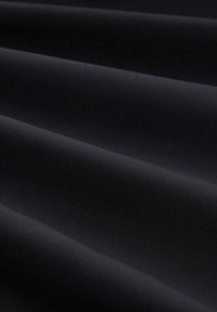 Zwarte stof met een gladde, licht gestructureerde oppervlakte, met platte plooien die zachte schaduwen creëren en de monochrome kleur benadrukken.