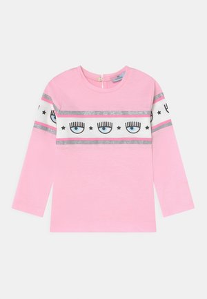 Chemise à manches longues rose clair avec une bande blanche et argentée ornée de motifs d'œil et d'étoile. Encolure ronde avec une fermeture à bouton au dos.