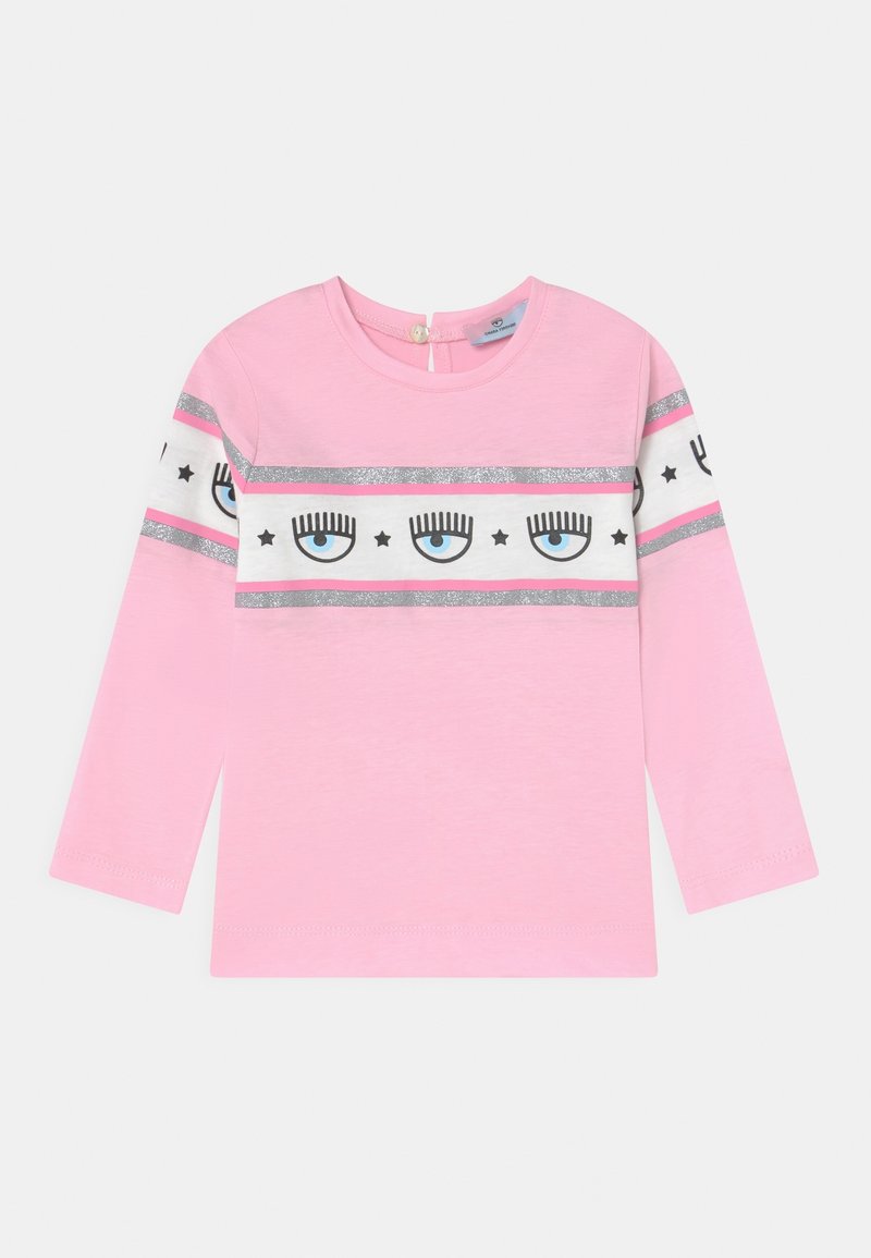 Lichtroze shirt met lange mouwen en een witte en zilveren streep met oog- en sterpatronen. Ronde halslijn met een knoopsluiting aan de achterkant.