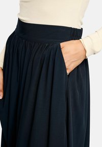 Söt�ét tengerészkék szoknya, széles, elasztikus derékpánttal, puha redőkkel és oldalzsebekkel, könnyű, lebegő anyagból készült.