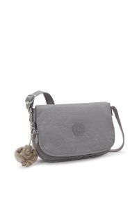 Bolso cruzado gris con correa ajustable, tapa frontal con cierre de cremallera y un pequeño llavero de mono de peluche adjunto.