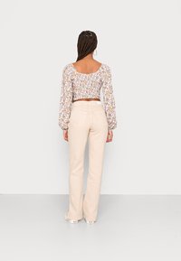 Blusa floral cropped com mangas longas e bufantes, apresentando as costas franzidas. Combinada com calças flare em bege claro com bolsos traseiros.