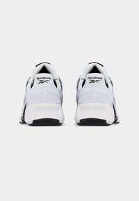 Ζεύγος λευκών αθλητικών παπουτσιών Reebok, εμφανιζόμενα από πίσω, με μαύρες σόλες και άνω μέρος από δίχτυ σε απλό φόντο.