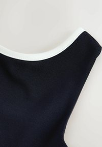 Približni prikaz mornarsko plave tkanine glatke teksture s bijelim rubom na odjevnom predmetu na svijetloj pozadini.