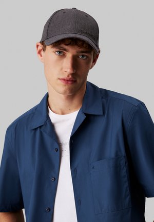 Gray cap with curved brim, textured fabric, and logo. Navy short-sleeve button-up shirt, smooth texture, featuring a chest pocket.