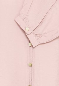 Light pink long-sleeve shirt cuff with pleats and a button, featuring a row of small textured gold buttons along the front.