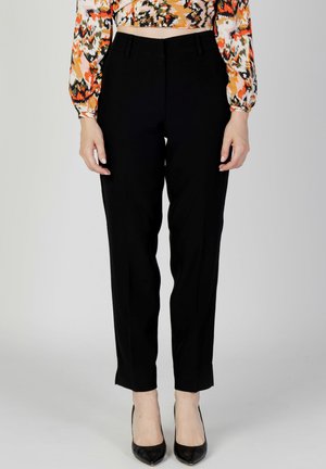 Pantalons noirs ajustés à jambe droite, taille haute et subtils plis latéraux, associés à des escarpins noirs à bout pointu.