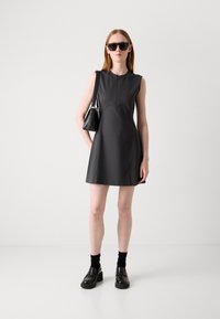 Grey sleeveless dress with a front zipper and A-line shape. Worn with black chunky shoes, black socks, and dark sunglasses. Black handbag.