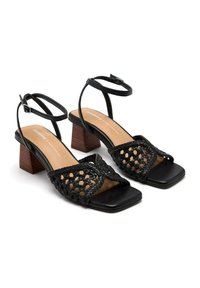 Sandales à talons noirs avec une bande supérieure tissée, un bout carré et un talon block. Bride de cheville avec une boucle décorative. Semelle intérieure en cuir lisse.