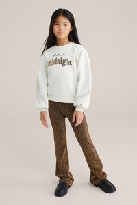 Fehér pulóver "Midnight" felirattal, puffos ujjal, barna texturált harangnadrággal és fekete platform cipőkkel párosítva.