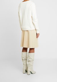 Sudadera de crema, falda beige y botas largas hasta la rodilla de estilo holgado con tacones gruesos. Texturas de tela suaves y ajuste casual.