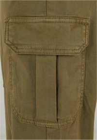 Beige Cargo-Hose aus Stoff mit einer rechteckigen Tasche mit Klappe und Falten, verstärkten Nähten an den Kanten, glatter Textur.