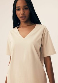 Beżowa bawełniana koszulka z krótkim rękawem i dekoltem w serek, o luźnym kroju i gładkiej fakturze.