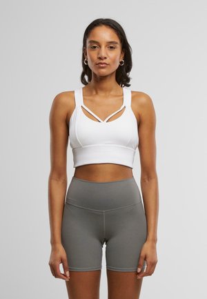 Hvit sports-bh med utskjæringsdesign og brede stropper, sammen med høy midje grå shorts. Glatt tekstur, tettsittende fasong.