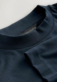 Marineblaue Baumwoll-T-Shirt mit rundem Ausschnitt, kurzen Ärmeln und glatter Textur; mit einem Etikett, auf dem "WEIHNACHTEN" steht.