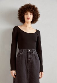 Un body negro de manga larga con un escote amplio, combinado con una falda de mezclilla oscura de cintura alta que presenta bolsillos frontales y botones.