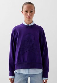 Paarse sweatshirt met een doodskop en kruisbotten ontwerp. Beschikt over een ronde halslijn, ribgebreide manchetten en zacht materiaal, gelaagd over een lichtblauw shirt.