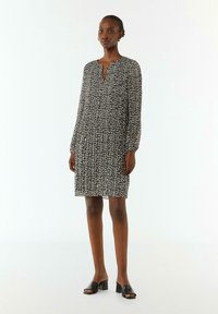 Leopardenmuster-Kleid mit knopflosem Ausschnitt, langen Ärmeln und lockerer Passform. Das Model trägt schwarze offene Blockabsatzschuhe.