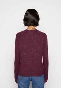 Pull bordeaux en tissu tricoté doux, avec un col rond et des manches longues, avec une coupe décontractée et un détail de bord-côte à l'ourlet.