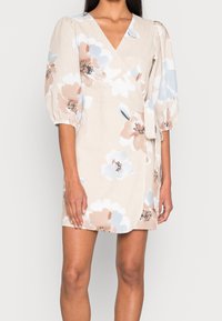 Blommig omlottklänning i beige med blå och persika mönster. Har puffärmar, V-ringning och textilerad tyg. Korts modell med sidoknyte.