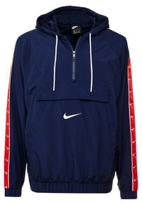 Marinblå Nike-hoodie vindjacka med halvdra ren, elastisk nederkant, vitt logotyp på bröstet och röda accenter med vita logotyper på ärmarna.
