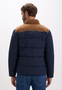 Giacca imbottita blu navy con colletto in suede marrone. Caratterizzata da un design a righe orizzontali, maniche lunghe e linea dritta. Contrasto di tessuti testurizzati.