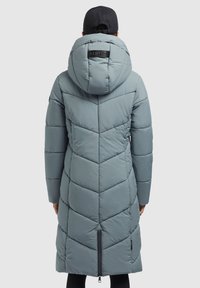 Svetlomodrý prešívaný kabát s kapucňou, chevron vzorom a bočnými zipsami. Pohľad zozadu zobrazuje detail loga na kapucni. Mäkšia textúra.