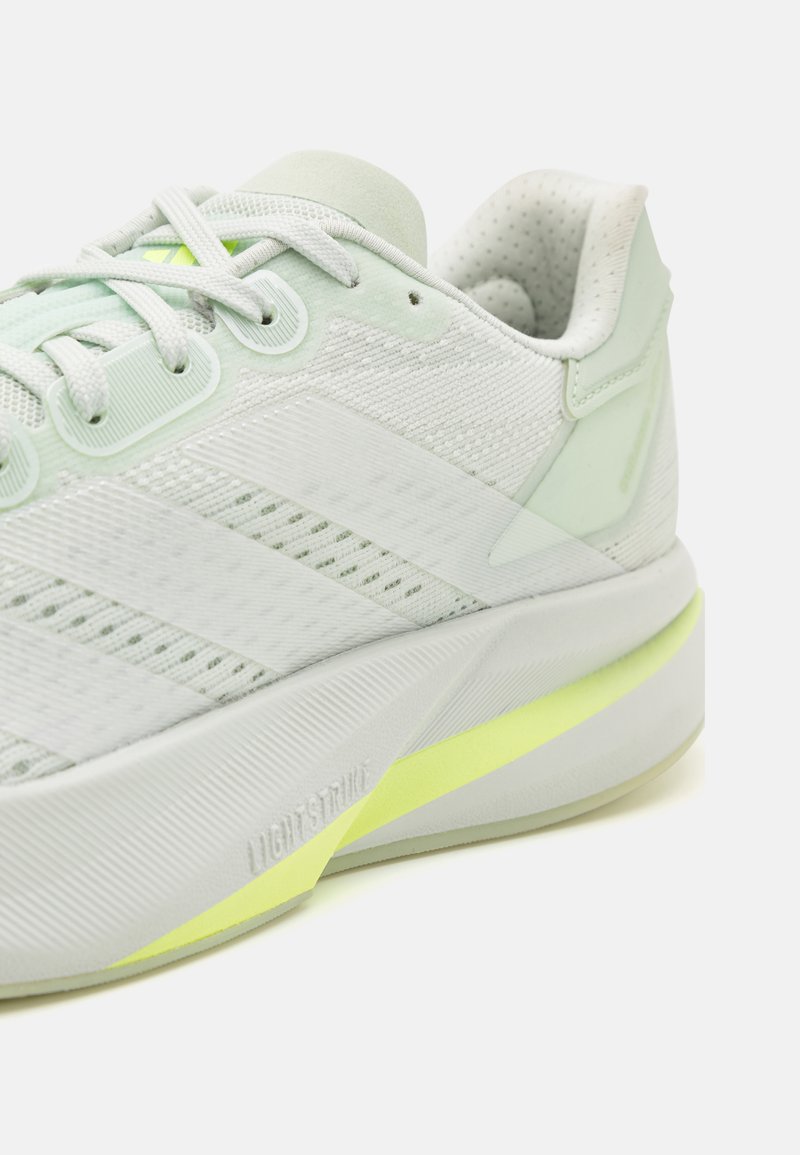 Hellgrüner Sportschuh mit einem strukturierten Mesh-Obermaterial, reflektierenden Akzenten und einer gepolsterten Sohle mit einem gelben Detail.