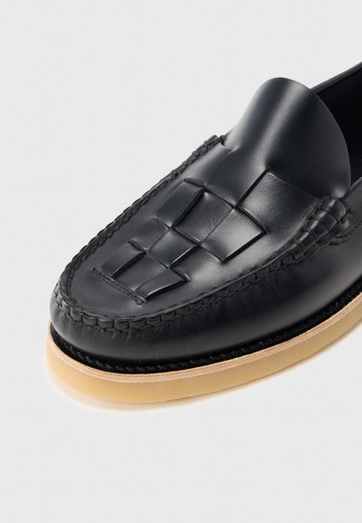 Mocasini negri din piele cu detaliu împletit pe partea superioară și talpă bej deschis, pe fundal alb.