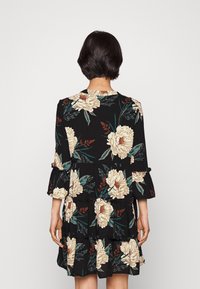 Abito floreale con sfondo nero, grandi rose beige e foglie verdi; maniche e orlo arricciati, con un design a strati.