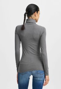 Maglione grigio a maniche lunghe con collo alto, dalla vestibilità aderente e dalla texture liscia, abbinato a jeans blu. La vista posteriore mostra una leggera curvatura all'orlo.