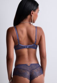 Ensemble de lingerie bleu marine composé de dentelle transparente, de motifs géométriques et de bords festonnés. Bretelles réglables et détail de quincaillerie décorative.