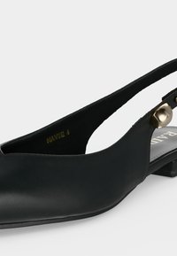 Mocassin noir en cuir avec bride arrière, détail bouton doré près de la cheville et petit talon carré.