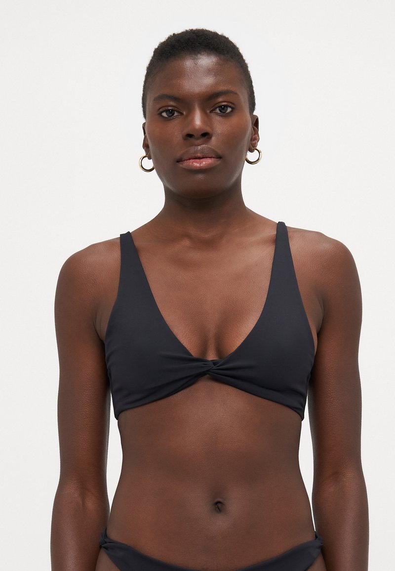 Fekete bikini felsőrész V-nyakú kialakítással, csavaros elülső résszel és vékony pántokkal. Simább anyagból készült, hangsúlyozva a minimalista stílust.