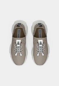 Un paio di sneakers beige di Steve Madden con suole chunky bianche e lacci elastici a bungee su sfondo bianco.