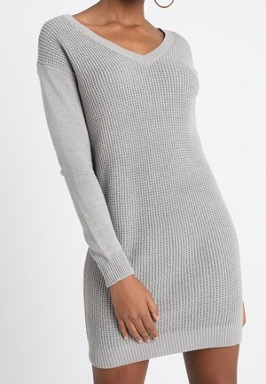 Long-sleeve, light gray knit sweater dress with V-neck worn by a standing person, showing textured fabric and ribbed cuffs.