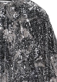 Chemise à sequins noire et argent avec un col, dotée d'une fermeture à boutons et d'une surface texturée et réfléchissante.