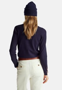 Námořnický pletený svetr s dlouhými rukávy, kulatým výstřihem a bočními rozparky, doplněný krémovými kalhotami a hnědým páskem.