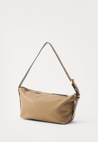 Sac à main synthétique beige avec une seule sangle réglable, forme rectangulaire, fermeture zippée et garniture noire contrastante le long des bords.