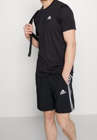 Svart atletisk t-shirt med korta ärmar och en vit logotyp, kombinerad med svarta shorts med vita ränder och logotyp på sidan.