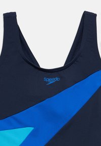 Μπλε ναυτικό μαγιό με μεγάλο μπλε φωτεινό στοιχείο, διαθέτει στρογγυλή λαιμόκοψη και χοντρές τιράντες. Το λογότυπο εμφανίζεται σε ανοιχτό μπλε μπροστά.