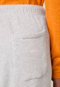 Lichtgrijze joggingbroek met een enkele achterzak, een zachte textuur en een elastische tailleband, gecombineerd met een oranje shirt met lange mouwen.