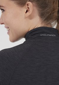 Mörkgrå träningsskjorta med hög krage, med en slät yta och "ENDURANCE"-logotypen broderad på baksidan.