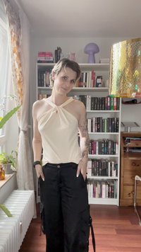 Top halter din crem cu detaliu împletit în față, asortat cu pantaloni cargo negri cu buzunare laterale și croială lejeră. Împrejurimi cu lumină naturală.