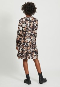 Robe à manches longues dans un imprimé abstrait noir, blanc et beige. Présente un ourlet en couches et un col rond, associée à des bottines noires.