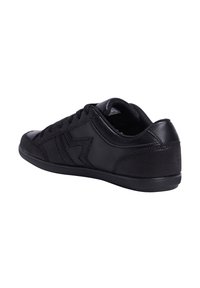 Zapatilla negra con parte superior de cuero suave y acentos de lona, con un perfil bajo, punta redonda y suela de goma plana.