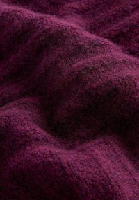 Gros plan sur un tissu en maille violet profond, doux et texturé, avec des fibres visibles et une surface légèrement duveteuse.