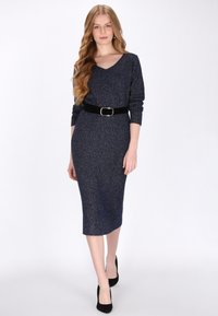 Tengerészkék kötött ruha V-kivágással, háromnegyedes ujjú, fekete övvel. Az anyag finom fénylő hatású és bordázott textúrájú.